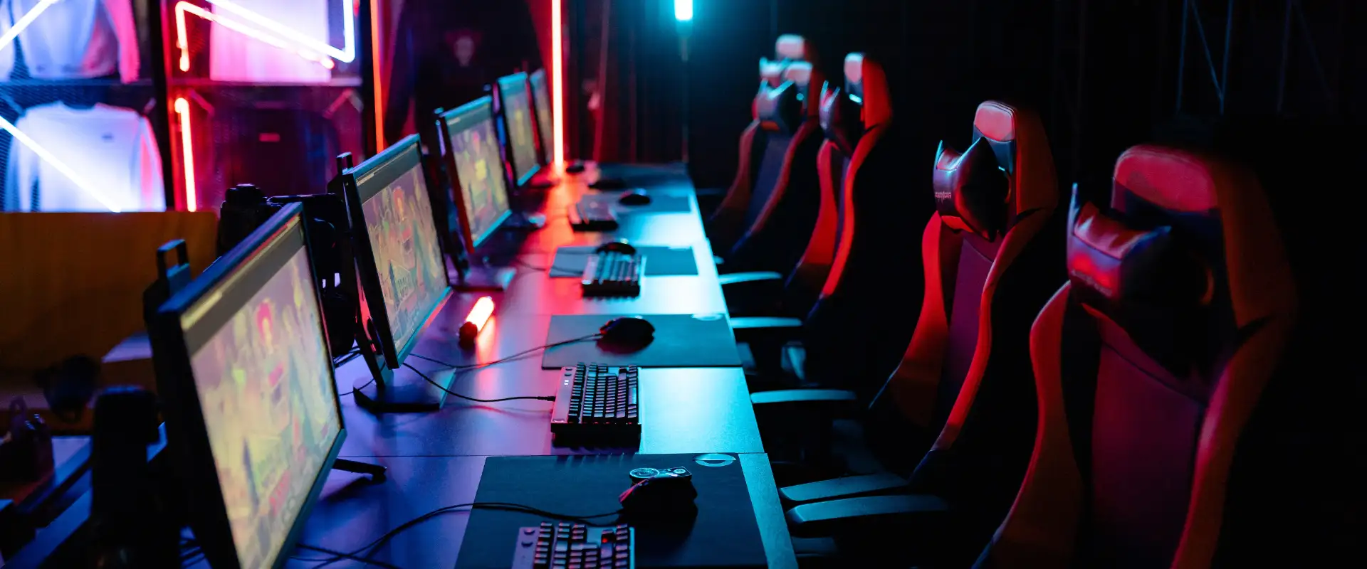 A row of desktop computers in a neon-lit gaming environment